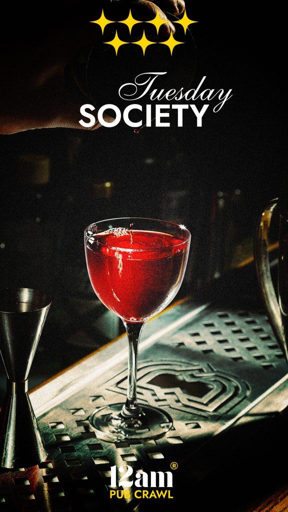 Tuesday Society Madrid Pub Crawl flyer featuring a vibrant red cocktail on a bar counter, with four gold stars and '12am Pub Crawl' logo. Experience Madrid's best Tuesday nightlife.