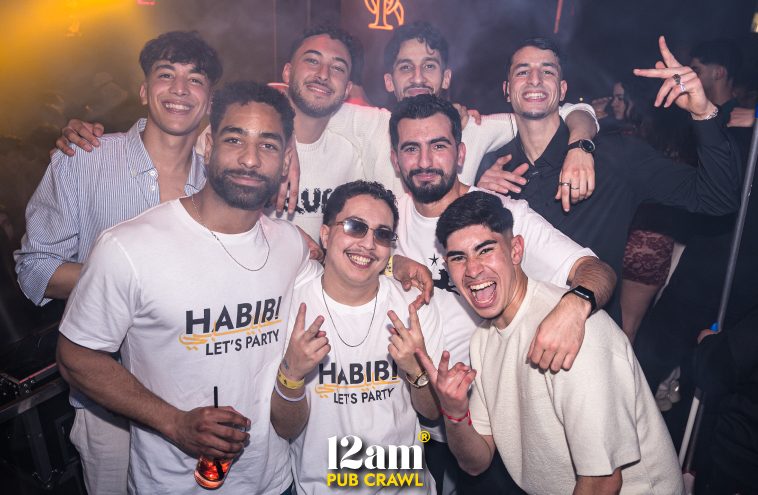 Group of excited young adults, including Erasmus students and solo travelers, posing with 12am Pub Crawl staff wearing "Habibi Let's Party" t-shirts at an Arabian night event in ICON Madrid Club. Showcasing the unique themed nightlife of a Madrid pub crawl.
