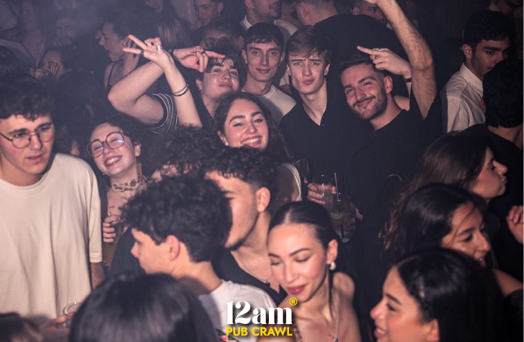 Large group of enthusiastic young adults, including Erasmus students and solo travelers, dancing and celebrating in a packed Madrid nightclub during a 12am Pub Crawl. Highlighting the ultimate party atmosphere.