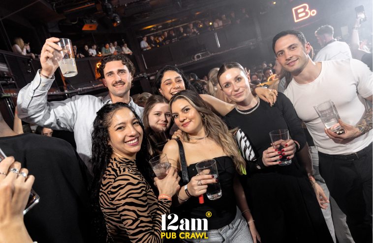 Diverse group of happy young adults, including Erasmus students and solo travelers, holding drinks and smiling at a bustling Madrid club during a 12am Pub Crawl. Capturing the vibrant and social Madrid nightlife experience.